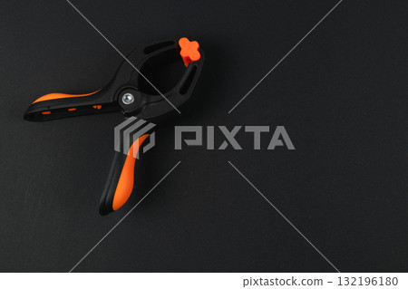 Black and orange clamp on dark surface with a smooth texture Black and orange clamp on dark surface with a smooth texture 132196180