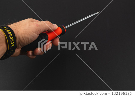 Hand holding a screwdriver ready for repair in a workshop setting Hand holding a screwdriver ready for repair in a workshop setting 132196185
