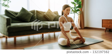 Young Asian woman meditating in lotus position at home Young Asian woman meditating in lotus position at home 132197382