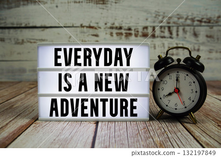 Everyday is a new adventure text with alarm clock on wooden background Everyday is a new adventure text with alarm clock on wooden background 132197849