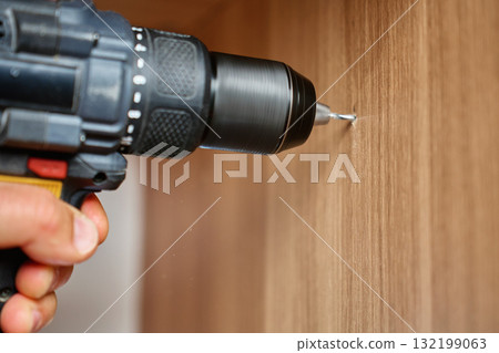 Close up of electric drill making hole in wooden furniture panel 132199063