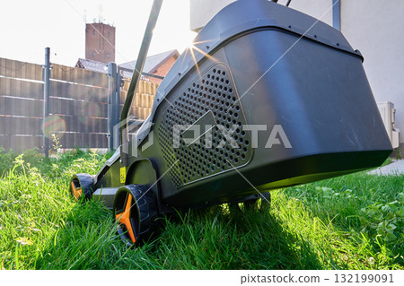 Electric lawn mower cutting grass in backyard Electric lawn mower cutting grass in backyard 132199091