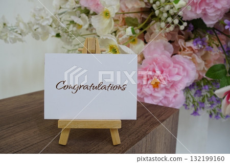 Congratulations text write on paper card with wooden easel and flowers decoration on wooden background Congratulations text write on paper card with wooden easel and flowers decoration on wooden background 132199160
