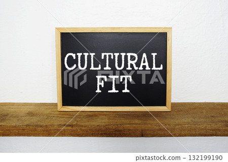 Cultural Fit text written on blackboard with wooden shelf and concrete background 132199190