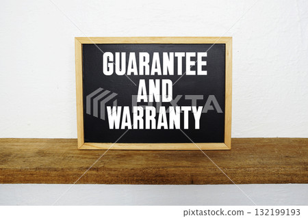 Blackboard with text "Guarantee And Warranty" on a wooden shelf, set against a white wall. 132199193