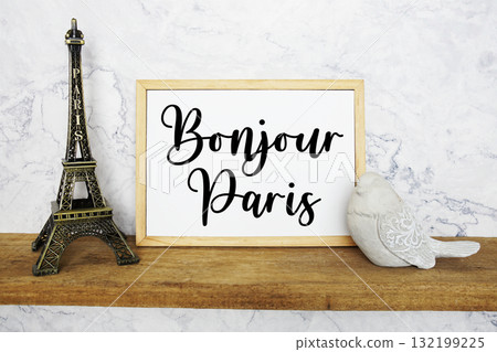 Bonjour Paris text written on whiteboard with Eiffel Tower Souvenir and bird statue on wooden shelf 132199225