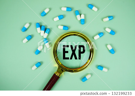 Expiration Date of Medicament with magnifying glass and medicine capsule on green background 132199233