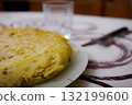 Homemade Spanish omelette on a white plate with a glass in the background 132199600