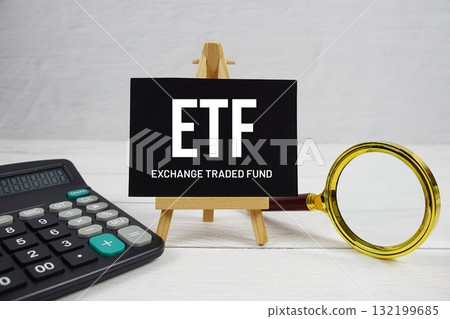 ETF abbreviation of Exchange Traded Fund text with magnifying glass and calculator on wooden background 132199685