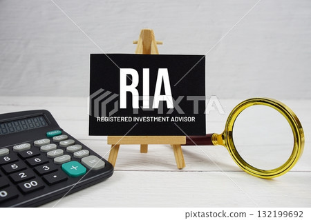 RIA abbreviation of Registered Investment Advisor text with magnifying glass and calculator on wooden background 132199692