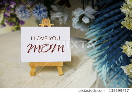 Happy Mother's day with I love you, MOM text write on paper card with wooden easel and flowers decoration on wooden background 132199717