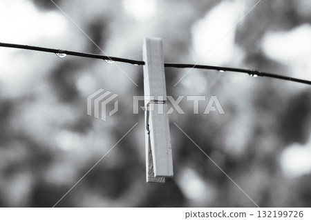 Minimalist black and white photo of a clothespin with raindrops on a wire 132199726