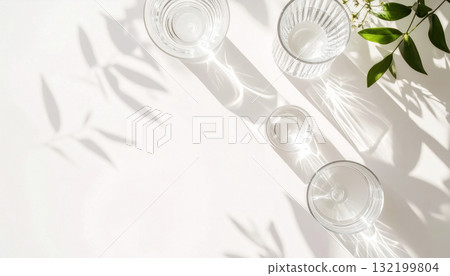 A minimal top-down composition of transparent glasses of water with long leaf shadows. A minimal top-down composition of transparent glasses of water with long leaf shadows. 132199804
