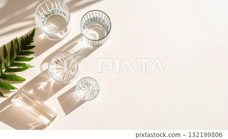A minimal top-down composition of transparent glasses of water with long leaf shadows. 132199806