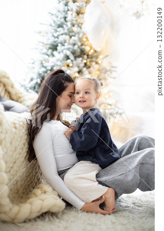 A tender moment between a mother and her daughter, sharing a loving embrace in front of a Christmas tree. A tender moment between a mother and her daughter, sharing a loving embrace in front of a Christmas tree. 132200149