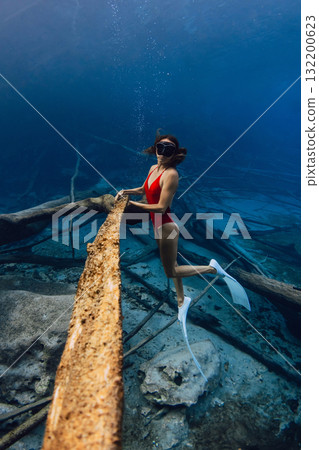 Woman freediver underwater holding sunken wooden log in the lake. Freediving in blue crystal lake 132200623