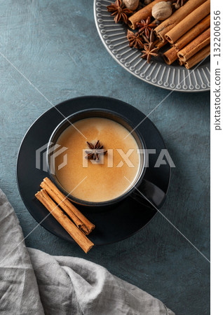 Traditional Indian masala chai tea with milk and spices in a black cup on a dark background  132200656