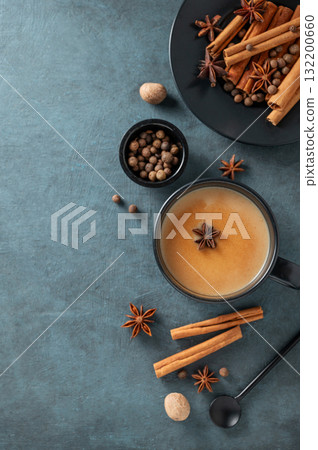 Traditional Indian masala chai tea with milk and spices in a black cup on a dark background 132200660