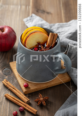 A cup of red mulled wine with spices, orange, apple slices and cranberry on a wooden background 132200668