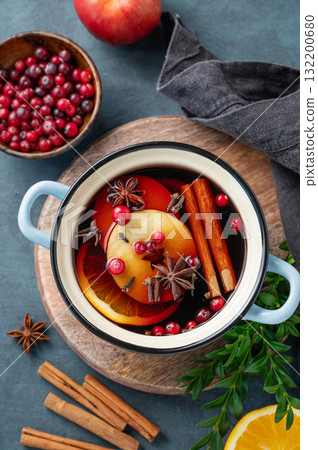 A pot of red mulled wine with spices, orange, apple slices, and cranberries on a wooden board A pot of red mulled wine with spices, orange, apple slices, and cranberries on a wooden board 132200680