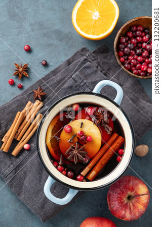 A pot of red mulled wine with spices, orange, apple slices, and cranberries on a dark  background 132200681