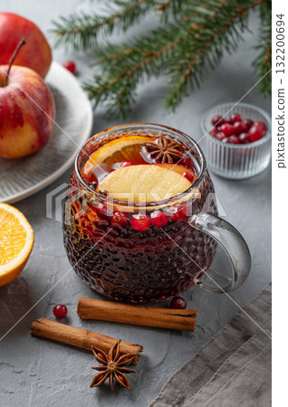 A cup of red mulled wine with spices, orange, apple slices and cranberry on a gray background 132200694