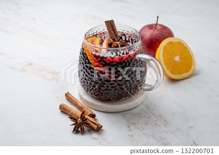 A cup of hot mulled wine with spices, orange and apple slices on a marble background A cup of hot mulled wine with spices, orange and apple slices on a marble background 132200701