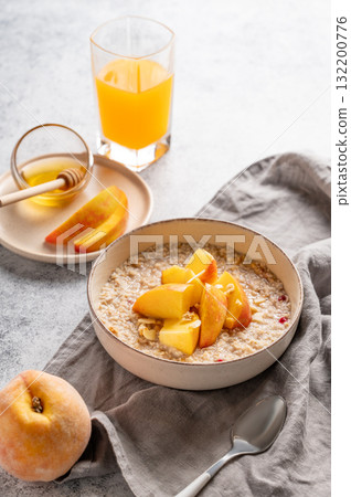 Oatmeal with peaches and nuts  in a bowl on a light background with honey 132200776