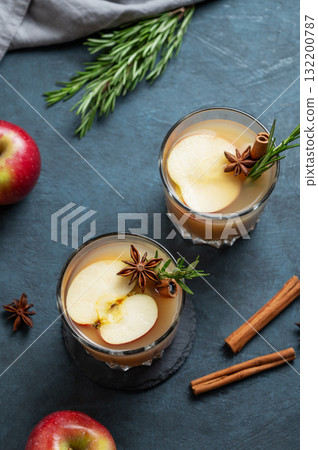 Two glassos of apple cider with cinnamon, anise, and rosemary on a dark blue background Two glassos of apple cider with cinnamon, anise, and rosemary on a dark blue background 132200787