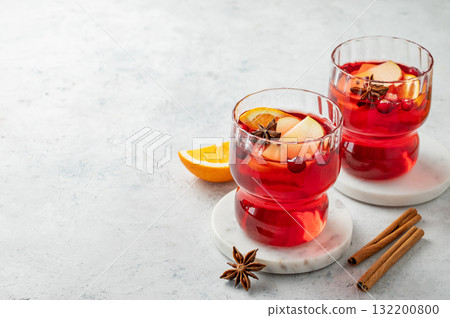 A cranberry drink in a two glasses on a light background with cinnamon and citrus fruit. A cranberry drink in a two glasses on a light background with cinnamon and citrus fruit. 132200800