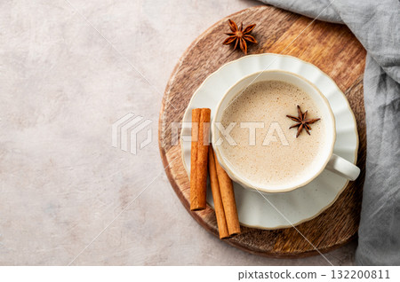 Traditional Indian masala chai tea with milk and spices in a white cup on a wooden board Traditional Indian masala chai tea with milk and spices in a white cup on a wooden board 132200811