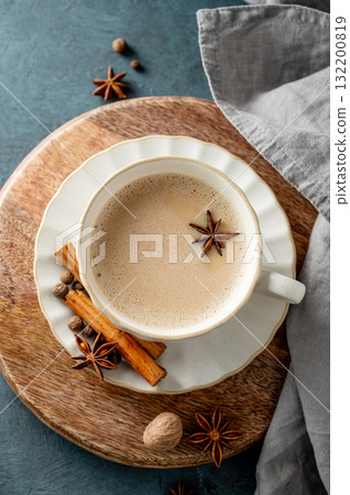 Traditional Indian masala chai tea with milk and spices in a white cup on a wooden board Traditional Indian masala chai tea with milk and spices in a white cup on a wooden board 132200819