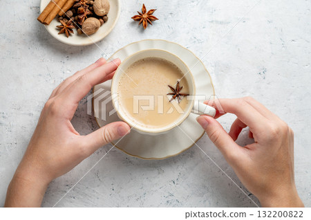 Hands holding traditional Indian masala chai tea with milk and spices in a white cup Hands holding traditional Indian masala chai tea with milk and spices in a white cup 132200822