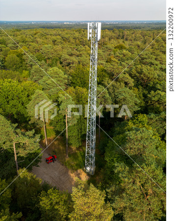 Aerial view of dense forest with a tall telecom tower and dirt access road highlighting the intersection of technology and natural landscape. Aerial view of dense forest with a tall telecom tower and dirt access road highlighting the intersection of technology and natural landscape. 132200972