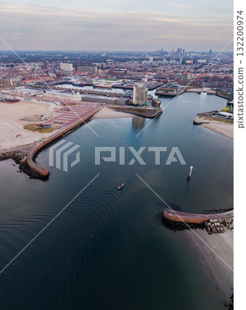 Hague, South Holland, Netherlands - 09.06.2025: Aerial view of coastal harbor with curved breakwaters, sandy beaches, boats, and dense cityscape showcasing urban planning, maritime infrastructure 132200974