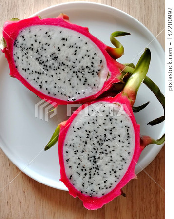 Top view of a fresh dragon fruit cut in half on a white plate. Top view of a fresh dragon fruit cut in half on a white plate. 132200992