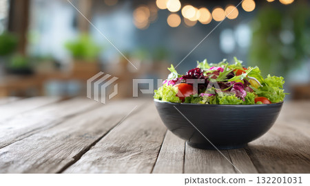 Fresh salad bowl with lettuce, tomato, and greens on rustic wooden table in cozy cafe 132201031