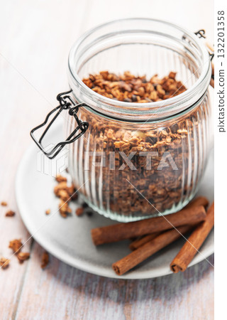 Granola cereal in glass jar with cinnamon sticks Granola cereal in glass jar with cinnamon sticks 132201358