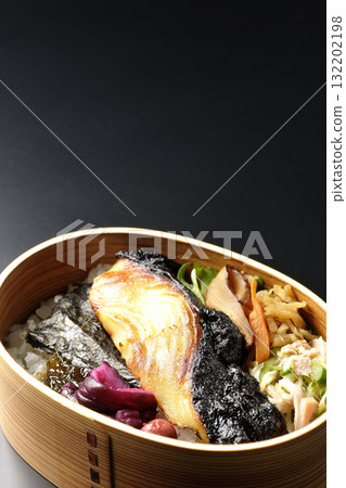 A bento lunch box with seaweed and grilled silver cod in a saikyo style sauce, photographed against a black background 132202198
