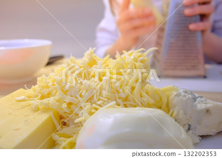 Woman rubs cheese on grater at home in the kitchen. Hands close-up. Woman rubs cheese on grater at home in the kitchen. Hands close-up. 132202353