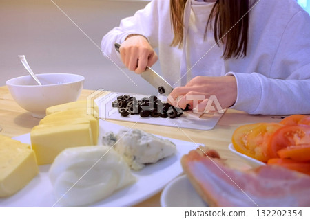 Woman cuts black olives on plastic board, hands close-up. Woman cuts black olives on plastic board, hands close-up. 132202354