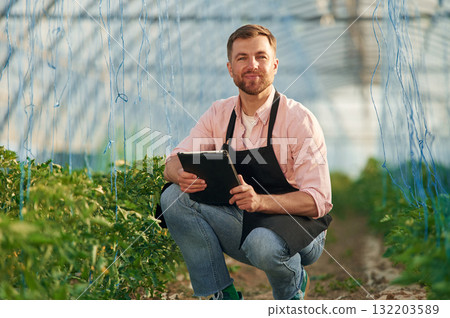Black digital tablet in hands. Man in greenhouse is working with plants Black digital tablet in hands. Man in greenhouse is working with plants 132203589