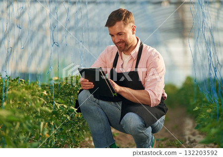 Reading the data. Man in greenhouse is working with plants Reading the data. Man in greenhouse is working with plants 132203592