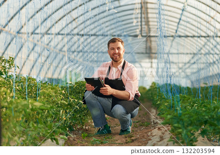 Black digital tablet in hands. Man in greenhouse is working with plants Black digital tablet in hands. Man in greenhouse is working with plants 132203594