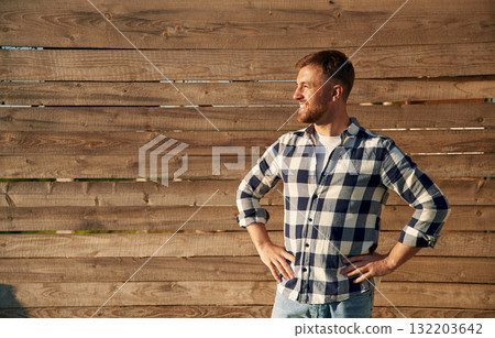 Man in checkered shirt is standing against wooden wall 132203642