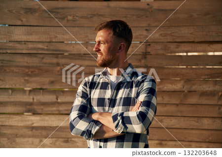 Man in checkered shirt is standing against wooden wall 132203648