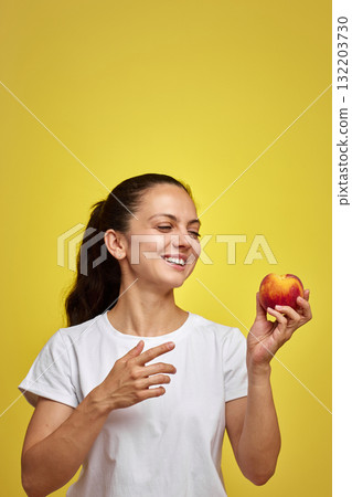 Happy woman holds peach fruit on yellow background Happy woman holds peach fruit on yellow background 132203730