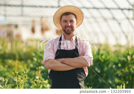 Smiling, in straw hat. Man in greenhouse is working with plants Smiling, in straw hat. Man in greenhouse is working with plants 132203993
