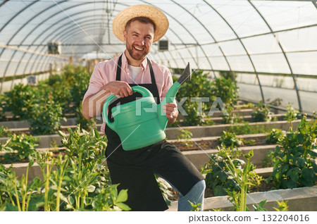 Watering can in hands. Man in greenhouse is working with plants 132204016