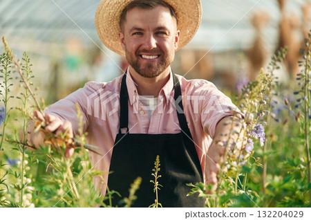 Cheerful facial expression. Man in greenhouse is working with plants Cheerful facial expression. Man in greenhouse is working with plants 132204029